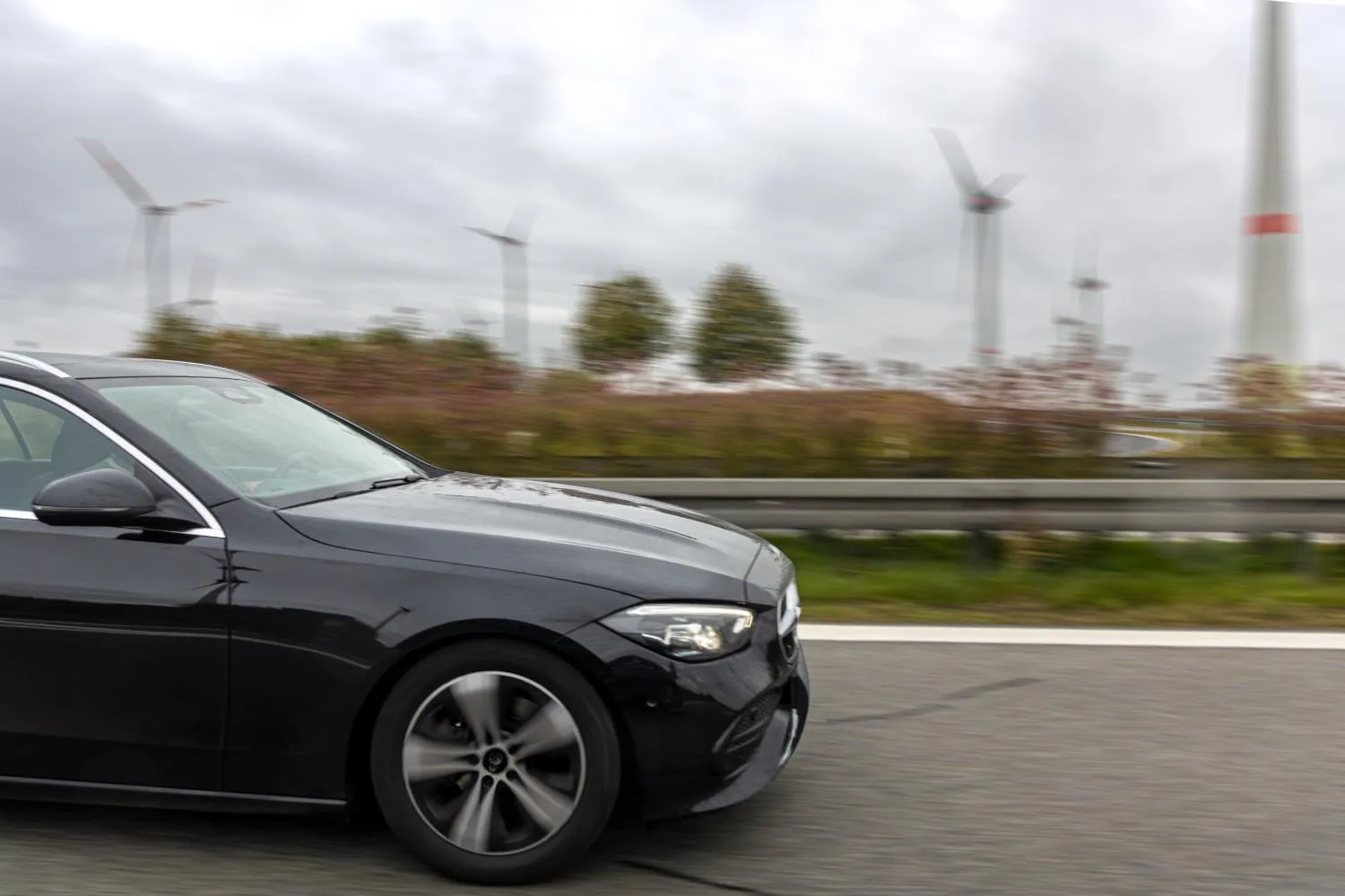 Black sedan driving along a highway past a row of wind turbines